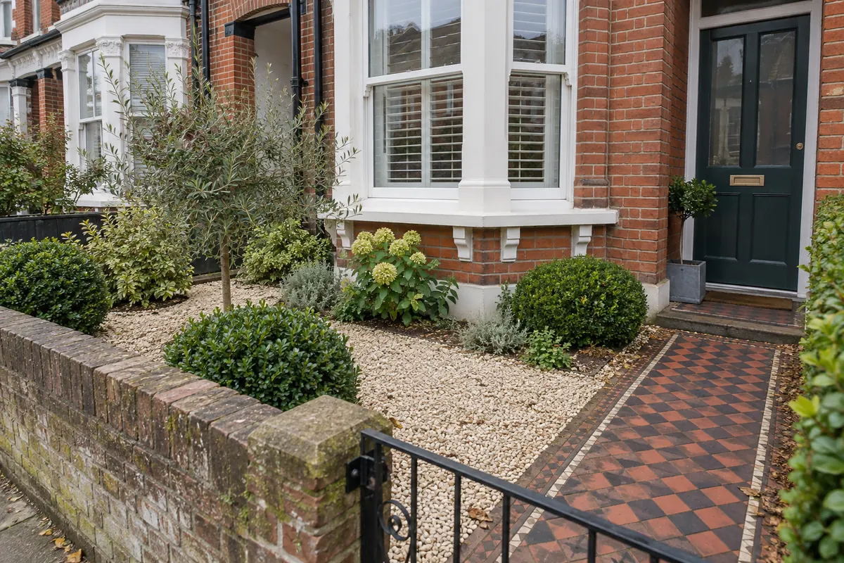 Small terraced-house front garden with cream gravel, repeated shrubs and a paved entrance path.